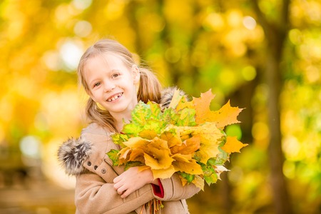 Portrait of adorable little girl with yellow leaves bouquet in fall at beautiful autumn dayの写真素材