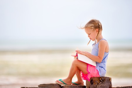Little adorable girl reading book during tropical white beachの写真素材