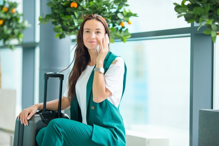 Portrait of young woman with smartphone in international airport. Airline passenger in an airport lounge waiting for flight aircraftの写真素材