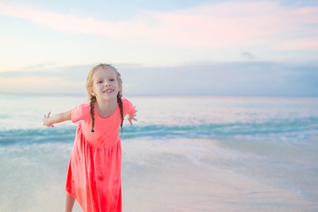 Adorable little girl at beach having a lot of fun in the evening. Happy kid looking at camera background beautiful sky and seaの写真素材