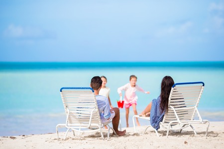Happy beautiful family of four on the beach. Parents relaxin on sunbed and kids having fun on the coastの写真素材