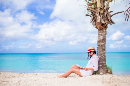 Young woman reading book during tropical white beachの写真素材