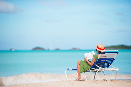 Young woman reading book on sunbeds during tropical white beachの写真素材