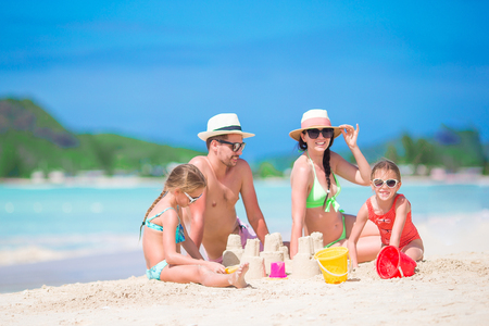 Family of four making sand castle at tropical white beachの写真素材