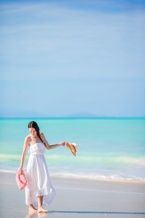 Young beautiful woman on white sand tropical beach. Caucasian girl with hat in dress background the seaの写真素材