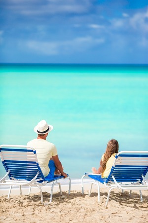 Father and daughter hands up on beach sitting on chaise-longueの写真素材