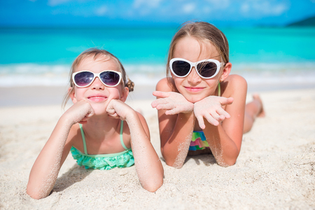 Adorable little sisters at beach during summer vacation lying on warm sand. Portrait of kids on white beachの写真素材