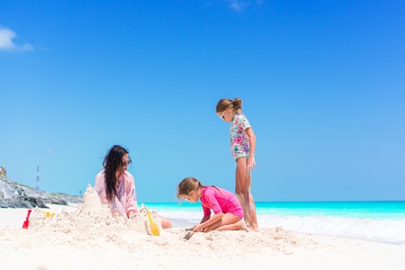 Family making sand castle at tropical white beach. Mother and two girls playing with sand on tropical beachの写真素材