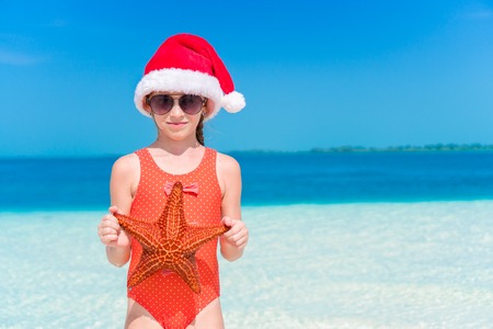 Adorable little girl with starfish on white empty beachの写真素材