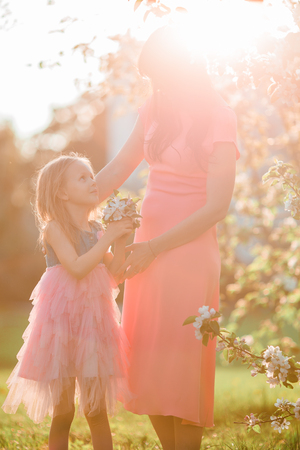 Adorable little girl with young mother in blooming cherry garden on spring dayの写真素材