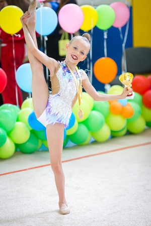 A beautiful little gymnast showing the medal and the cup won after a competitionの写真素材