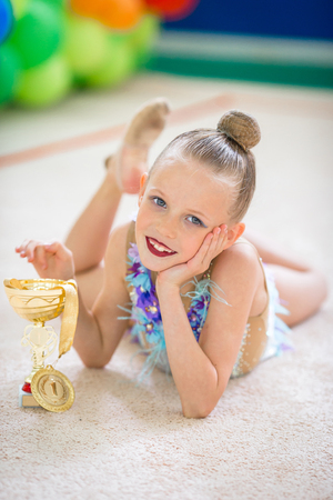 A beautiful little gymnast showing the medal and the cup won after a competitionの写真素材