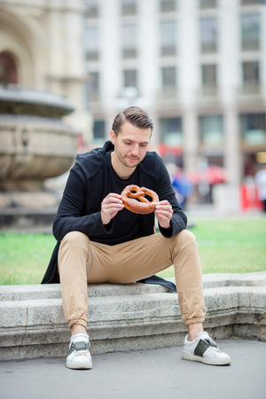 Beautiful young man holding pretzel and relaxing in parkの写真素材