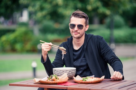 Young man eating take away noodles on the streetの写真素材