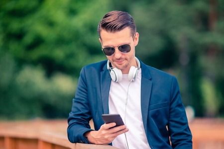 Man is reading text message on mobile phone while walking in the parkの写真素材