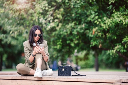 Cute woman is reading text message on mobile phone while sitting in the park.