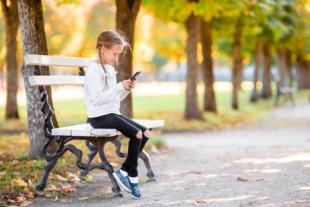 Little adorable girl with smartphone in fall.の写真素材