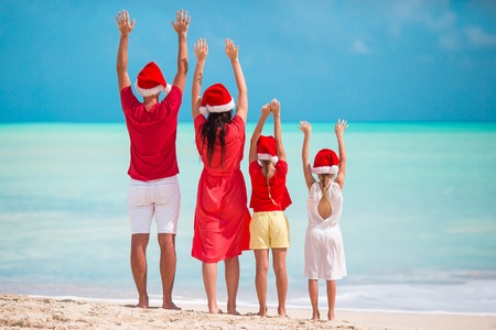 Happy family in red Santa hats on a tropical beach celebrating Christmas vacationの写真素材