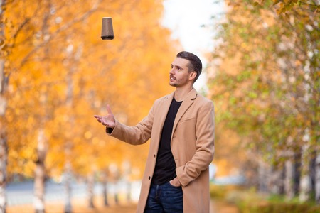 Young man drinking coffee with phone in autumn park outdoors