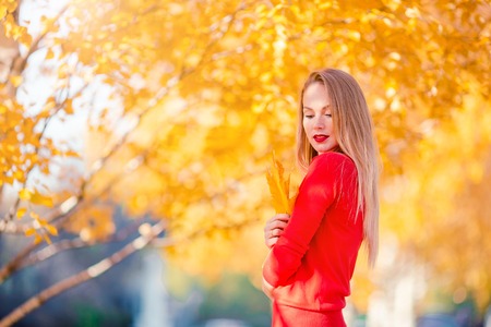 Fall concept - beautiful woman drinking coffee in autumn park under fall foliageの写真素材