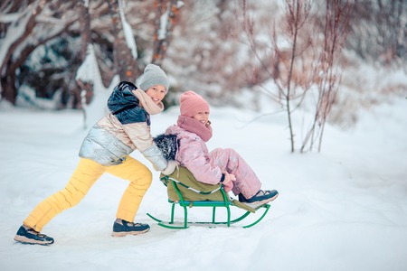 Adorable little happy girls sledding in winter snowy day.の写真素材