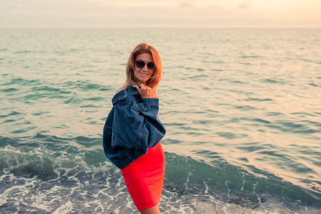 Outdoor fashion portrait of stylish girl wearing trendy sunglasses and jeans jacket on the beach. Hands up, retro filter, flecks of sunlightの写真素材