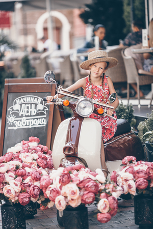 Adorable little girl in hat on the moped outdoorsの写真素材
