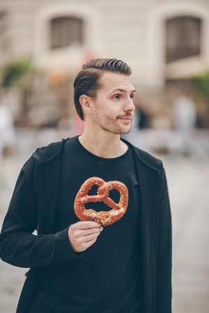 Beautiful young man holding pretzel and relaxing in parkの写真素材