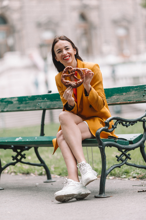 Beautiful young woman holding pretzel and relaxing in parkの写真素材
