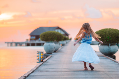 Silhouette of adorable little girl on wooden jetty at sunsetの写真素材