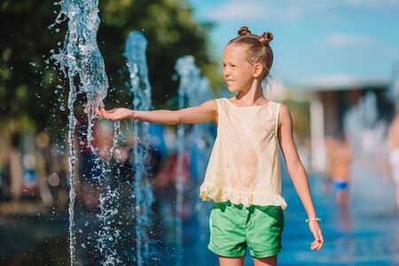 Little adorable girl have fun in street fountain at hot sunny dayの写真素材