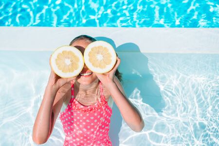 Little girl covering eyes with lemon halves near eyes on background swimming poolの写真素材
