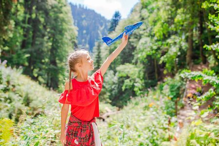 Happy little girl with toy airplane in hands in mountainsの写真素材