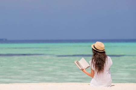 Portrait of a young woman relaxing on the beach, reading a bookの写真素材
