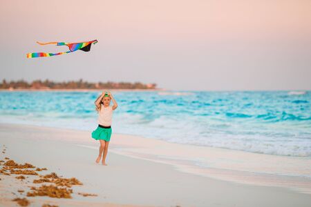 Little running girl with flying kite on tropical beach. Kid play on ocean shore.の写真素材