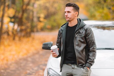 Young man drinking coffee with phone in autumn park outdoors