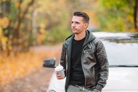 Young man drinking coffee with phone in autumn park outdoors