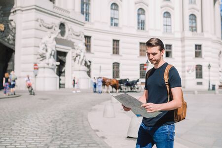 Man tourist with a city map and backpack in Europe street. Caucasian boy looking with map of European city.の写真素材