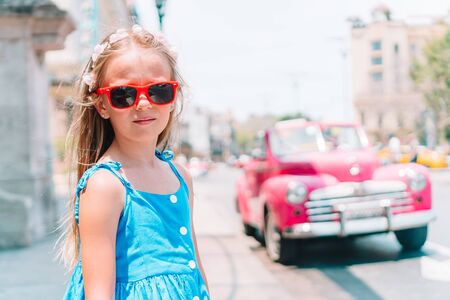 Adorable little girl in popular area in Old Havana, Cuba. Portrait of kid with vintage classic american carの写真素材