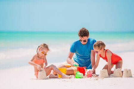 Father and two girls playing with sand on tropical beachの写真素材