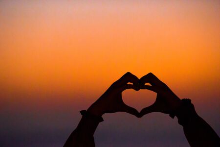 Silhouette of adorable little girl making the heart on a beach at sunsetの写真素材