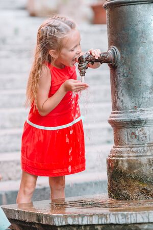 Little adorable girl drinking water from the tap outside at hot summer day in Rome, Italyの写真素材