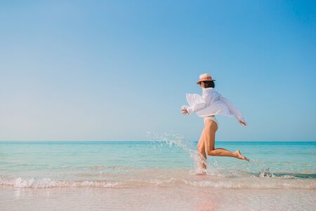 Young beautiful woman in hat and white shirt relaxing on the beach, splashing and having funの写真素材