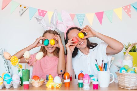 Mother and her little daughter have fun at Easter holiday. Family wearing bunny ears at homeの写真素材