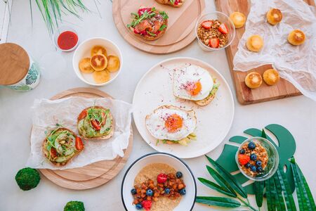 Healthy breakfast, morning porridge with fruits, bruschettas with avocado, fried eggs, granola and cheesecakes for big familyの写真素材