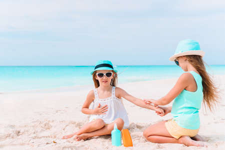 Little girl with bottle of sun cream sitting at tropical beach