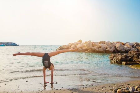 Little girl having fun at tropical beach during summer vacation at shallow water. Cute kid making sporty exercises on the seashoreの写真素材