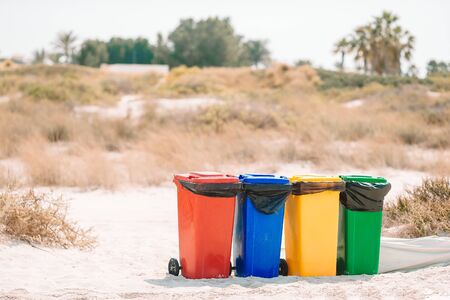 Bright plastic containers for garbage sorting on the beach. Red, yellow, blue and green containers for glass, plastic, wastes and paper on the sand beach on the seaside. Ecology and recycling conceptの写真素材