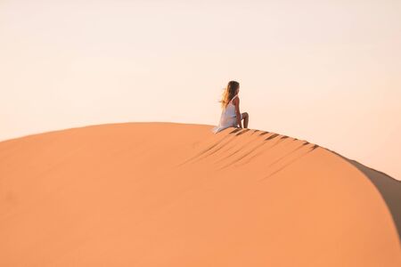 Little girl in white dress on vacation in big dunes in beautiful desertの写真素材