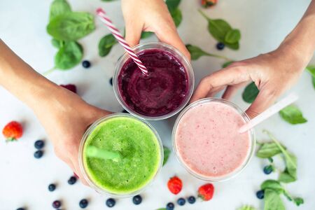 Row of healthy fresh fruit and vegetable smoothies with assorted ingredients. Assorted fruit shakes in hands closeup. Smoothie conceptの写真素材